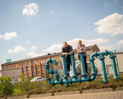 Zwei Mitarbeitende stehen auf einem SWM Logo aus Rohren gebaut