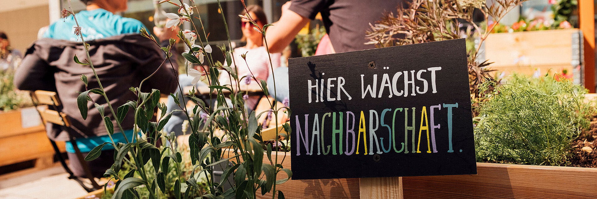 Blick in Nachbars Garten mit Schild "Hier wächst Nachbarschaft" im Vordergrund