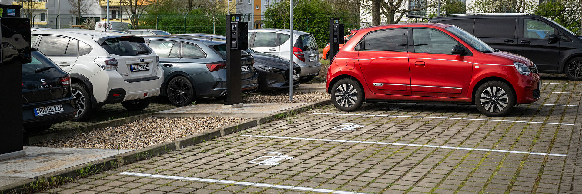 Blick auf einen Parkplatz mit E-Ladesäulen und einer Ladesäule tankt ein rotes Auto