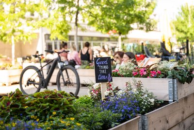 Beetschild "Good things take time" in Nachbars Garten mit Fahrrad im Hintergrund