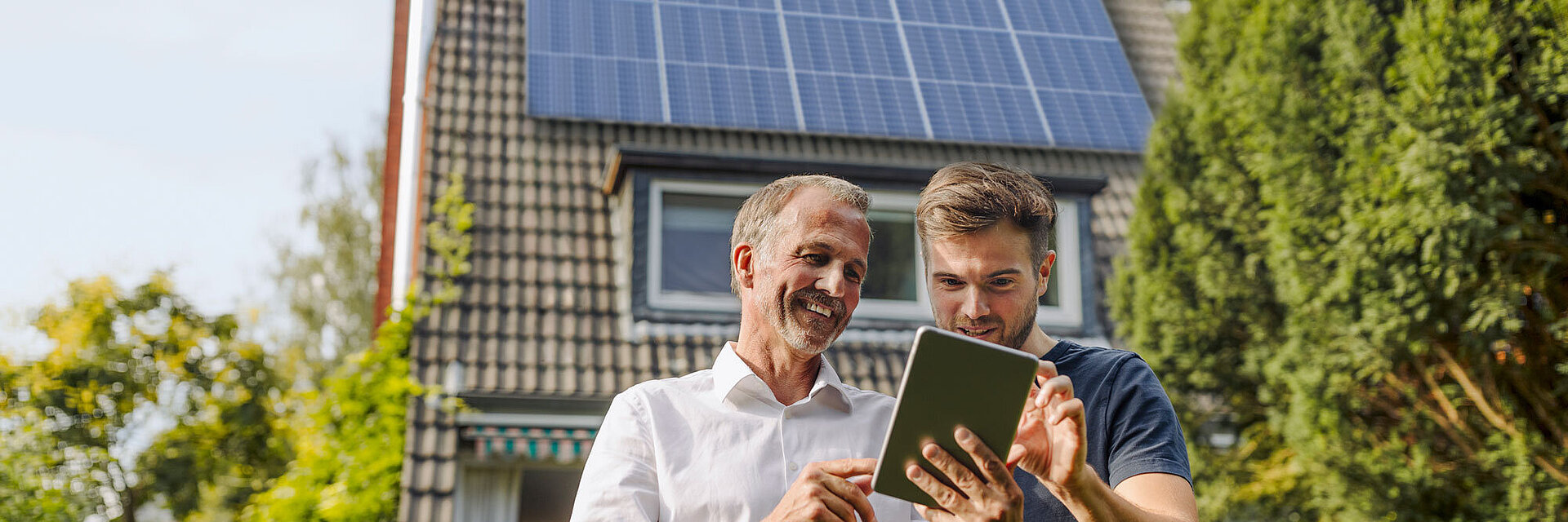 Zwei Männer stehen vor einem Haus mit PV Anlage und schauen auf ein Tablet