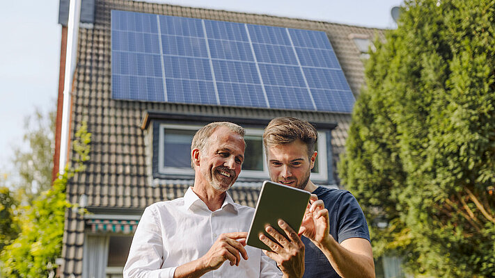 Zwei Männer stehen vor einem Haus mit PV Anlage und schauen auf ein Tablet