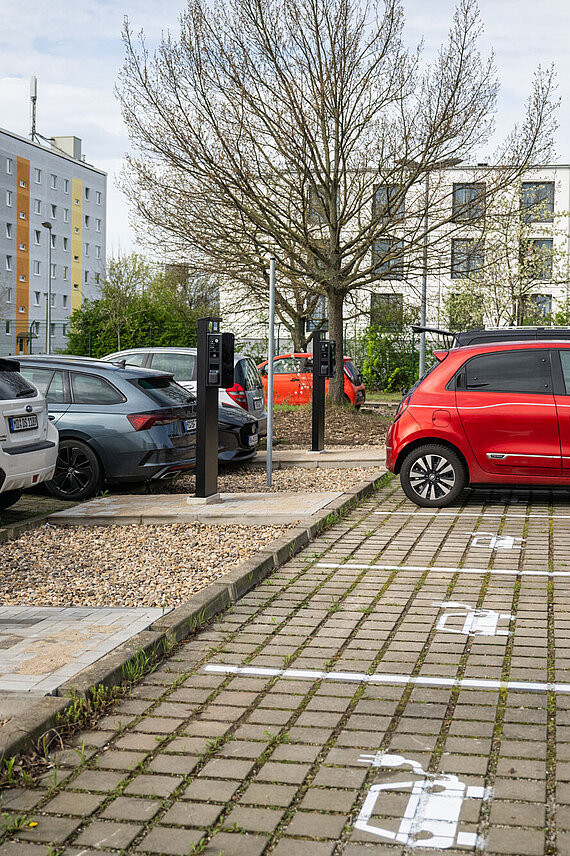 Blick auf einen Parkplatz mit E-Ladesäulen und einer Ladesäule tankt ein rotes Auto