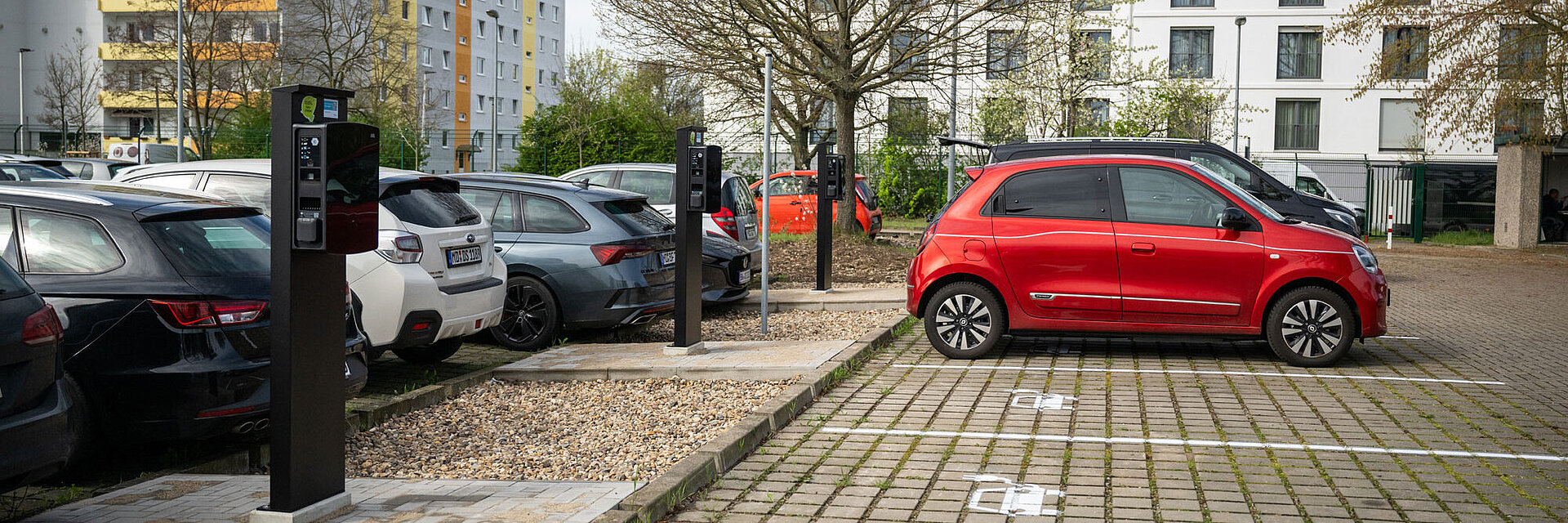 Blick auf einen Parkplatz mit E-Ladesäulen und einer Ladesäule tankt ein rotes Auto